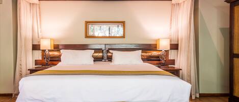 Un grand lit avec une tête de lit en bois, deux tables de chevet avec des lampes et un tableau encadré au-dessus du lit.