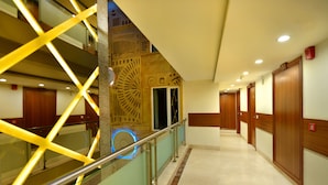 A hotel corridor with a modern design, featuring a glass railing, wooden doors, and a decorative wall with geometric patterns. - Hotel Regent Grand (New Delhi)