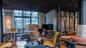 Een modern interieur met verschillende zithoeken, waaronder ronde tafels en banken, en grote ramen die voor natuurlijk licht zorgen.