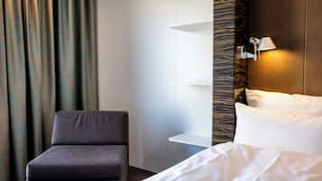 A hotel room with a bed, a chair, a nightstand, and a wall-mounted lamp.