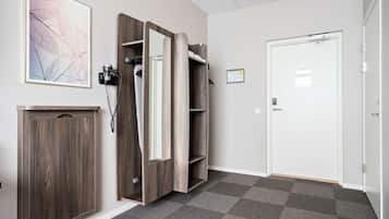 A hotel room with a wooden wardrobe, a coat rack, a framed abstract artwork, and a door with a small notice.