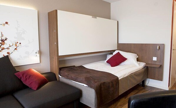 Ein kompaktes Hotelzimmer mit einem Einzelbett, einer Schlafcouch und einer kleinen Sitzecke.
