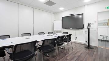 A conference room with a long table, black chairs, a flat-screen TV, and a whiteboard.
