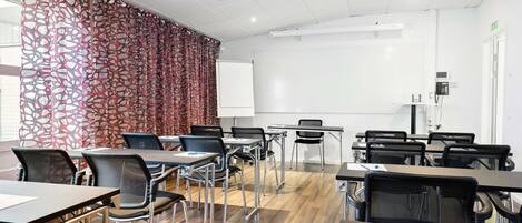 Un salón de conferencias con mesas, sillas, una pizarra y una cortina estampada.