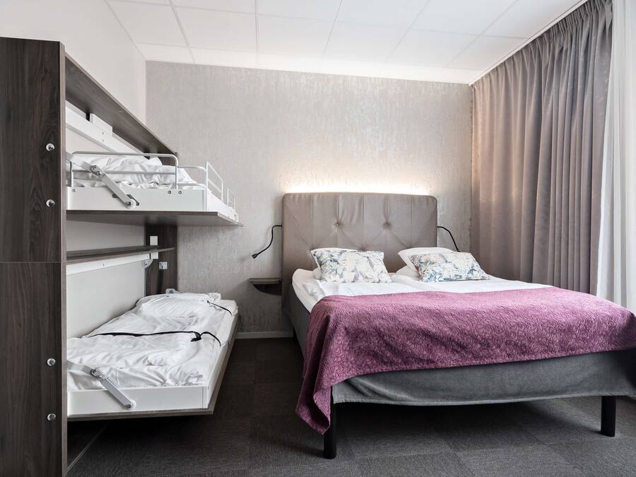 Habitación de hotel con literas, una cama individual, una mesita de noche y un ventanal grande con cortinas.