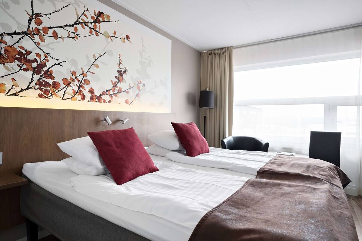 Une chambre d’hôtel avec deux lits, une grande fenêtre, une lampe et une œuvre d’art murale.