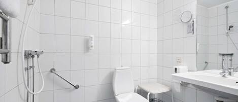 A modern bathroom with white tiles, a white toilet, a sink, and a shower.