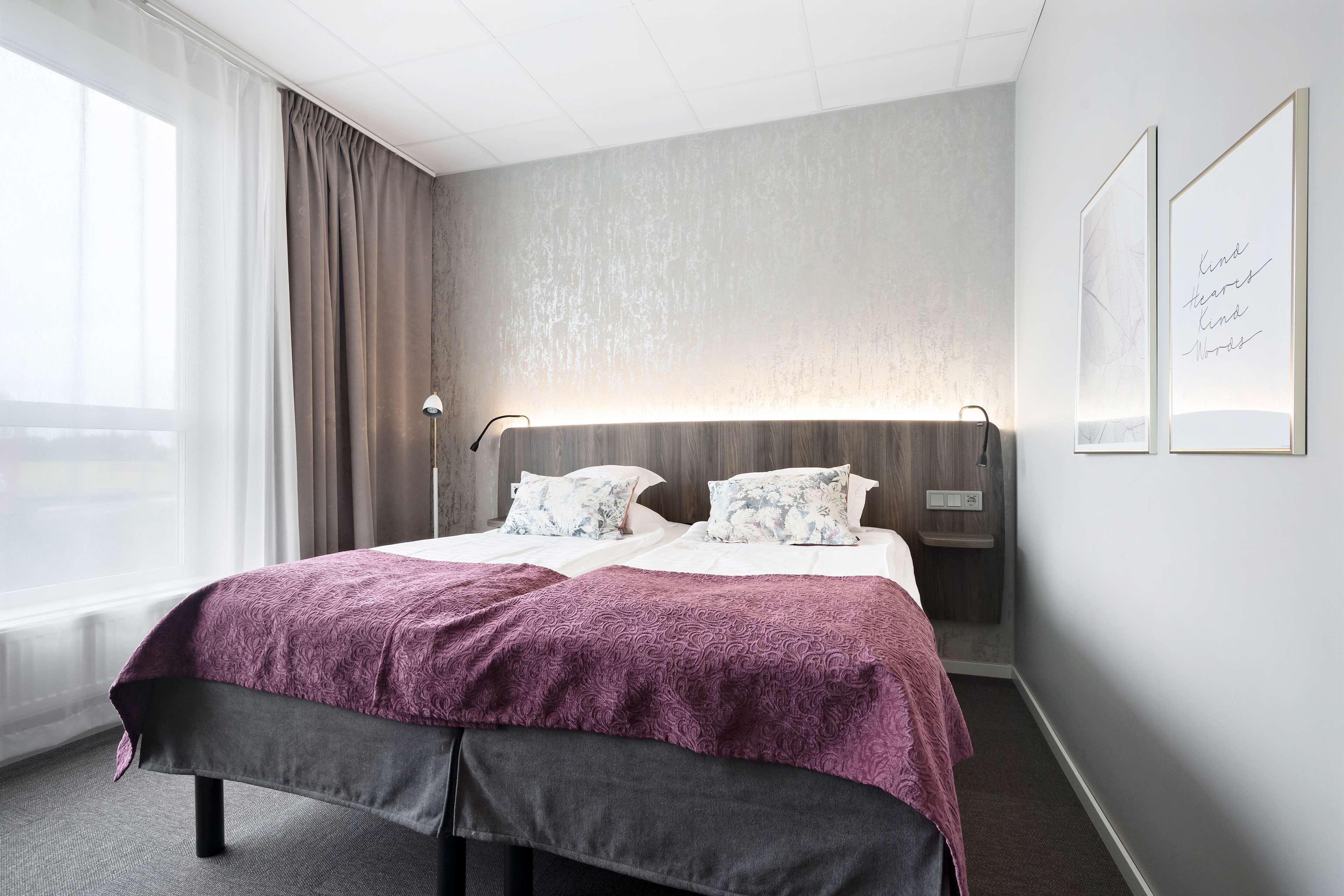 Une chambre d’hôtel moderne avec un grand lit, une table de chevet, une lampe et une fenêtre avec des rideaux.