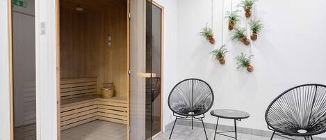 Ein Zimmer mit Sauna, zwei schwarzen Stühlen, einem kleinen Tisch und hängenden Pflanzen.
