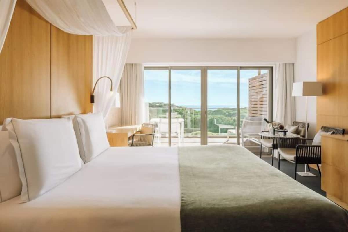 A hotel room with a large bed, a desk, a chair, and a view of the outdoors.