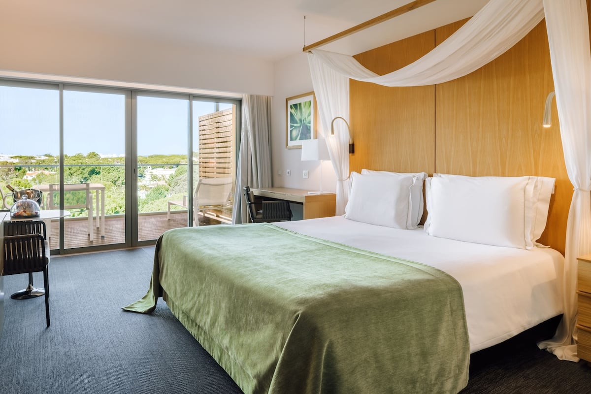 A hotel room with a large bed, a desk, a chair, and a view of the outdoors.