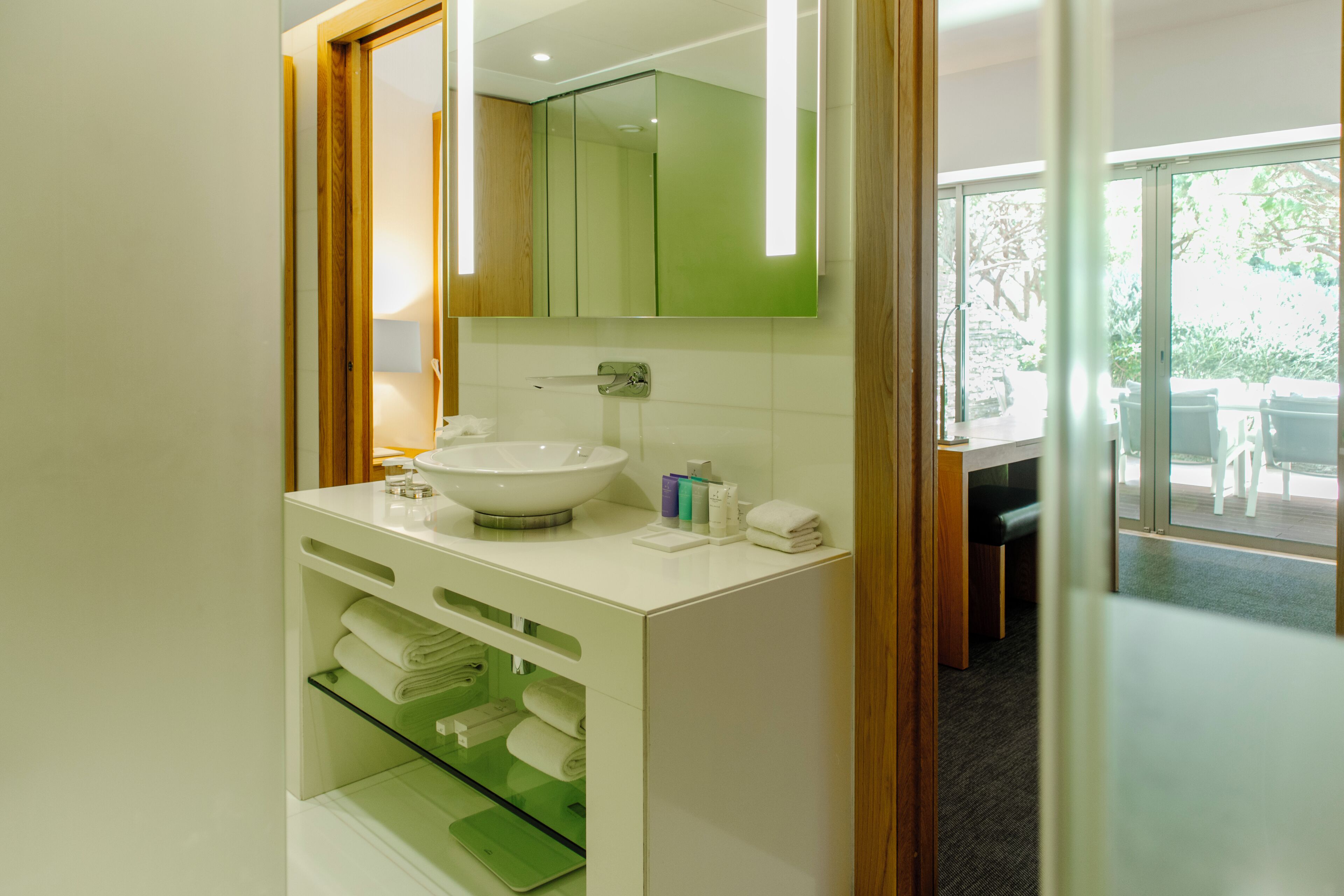 Un baño moderno con lavamanos blanco, espejo y repisas con toallas.