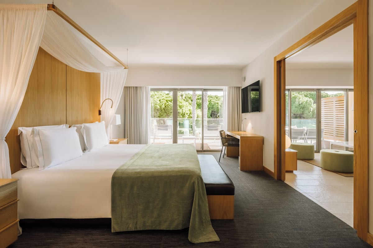 A hotel room with a bed, a desk, a TV, and a balcony with outdoor seating.