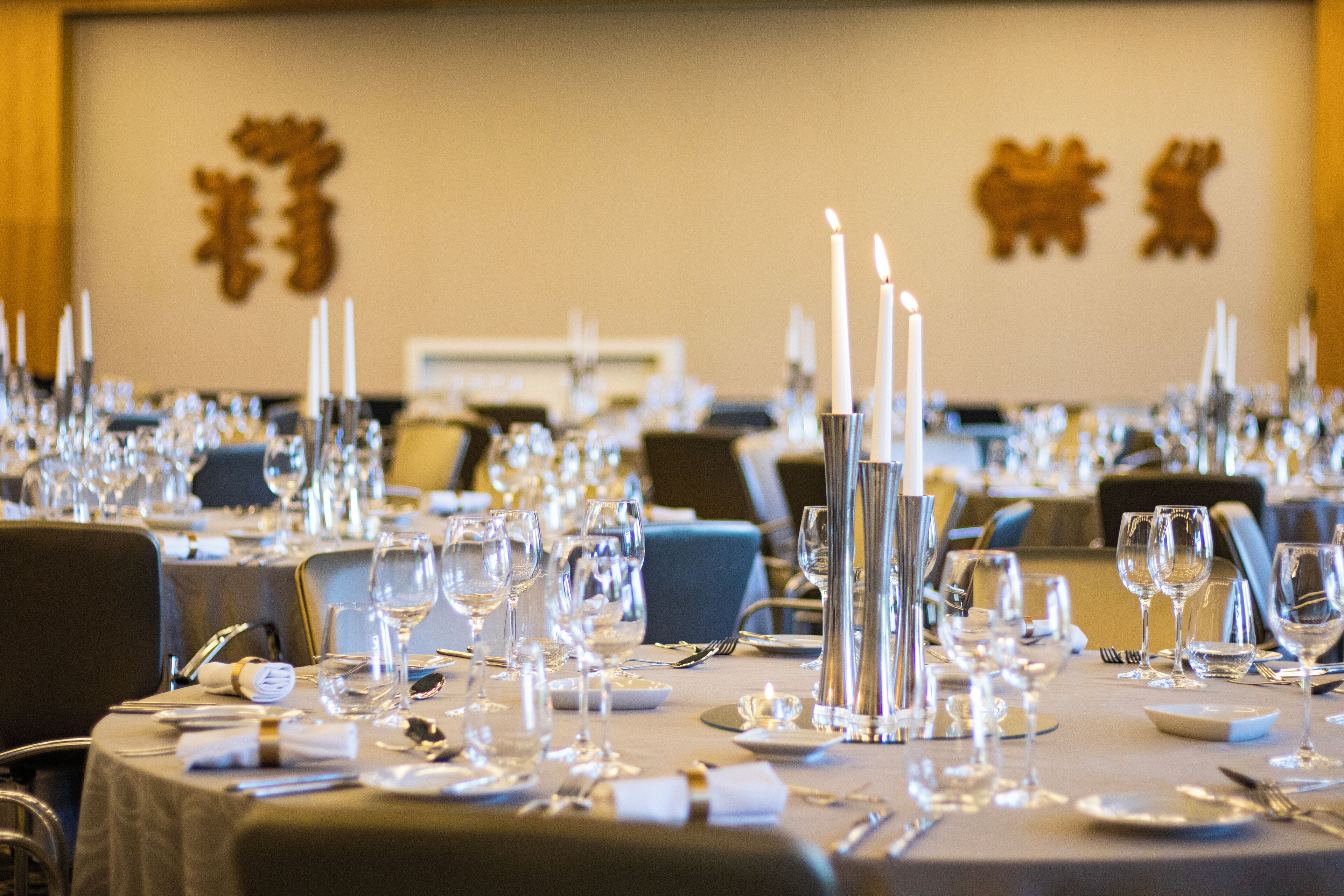 Une salle de banquet où les tables sont dressées pour un événement formel, avec des bougies, des verres à vin et des couverts.