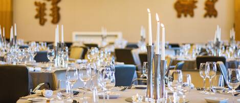 Une salle de banquet où les tables sont dressées pour un événement formel, avec des bougies, des verres à vin et des couverts.