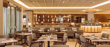 A modern hotel dining area with multiple seating options, including tables and booths, and a central bar area.