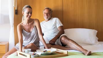 A couple sitting on a bed with a tray of food and a cup.