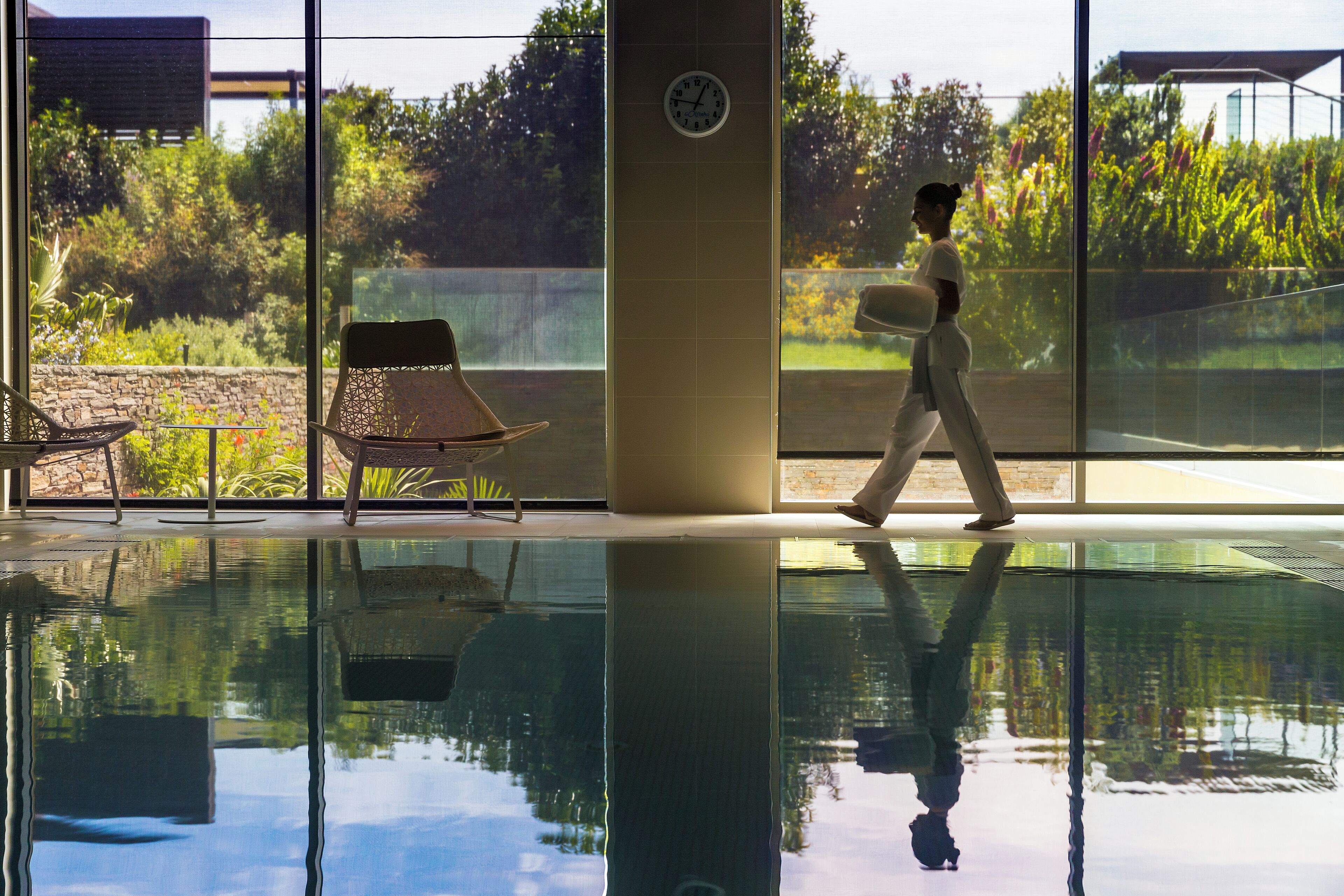 A pool area with a glass floor, a clock on the wall, and a chair.