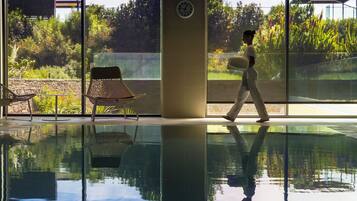 A pool area with a glass floor, a clock on the wall, and a chair.