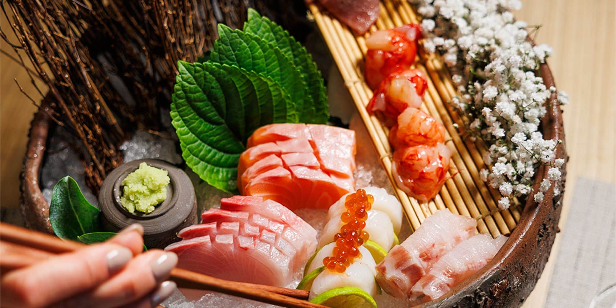 Diverse sushi en sashimi op een houten schaal, met stokjes, garnering en een kleine wasabi-kom.