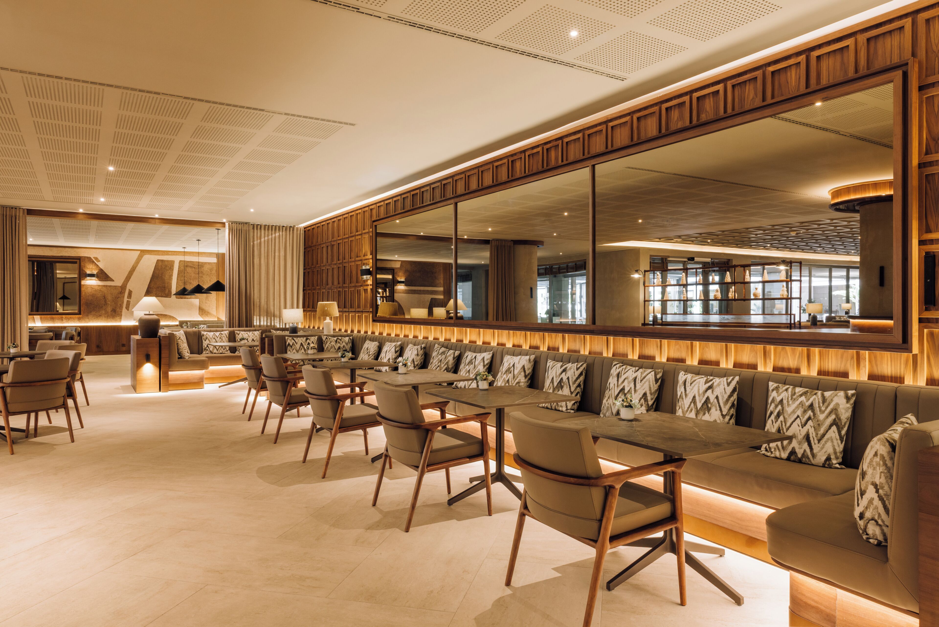 Un moderno vestíbulo de hotel con una amplia zona de estar, un bar y un gran espejo que refleja el interior.