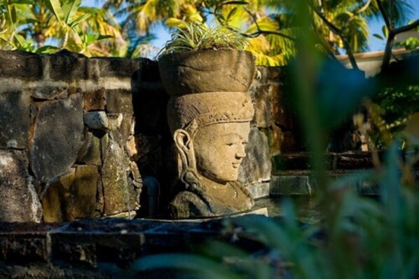 A stone structure with a carved face and a potted plant on top. - Oasis Villas by Fine and Country (Grand-Baie)