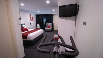 Una habitación de hotel con una cama, televisión montada en la pared, una cinta de correr y un escritorio con una silla.
