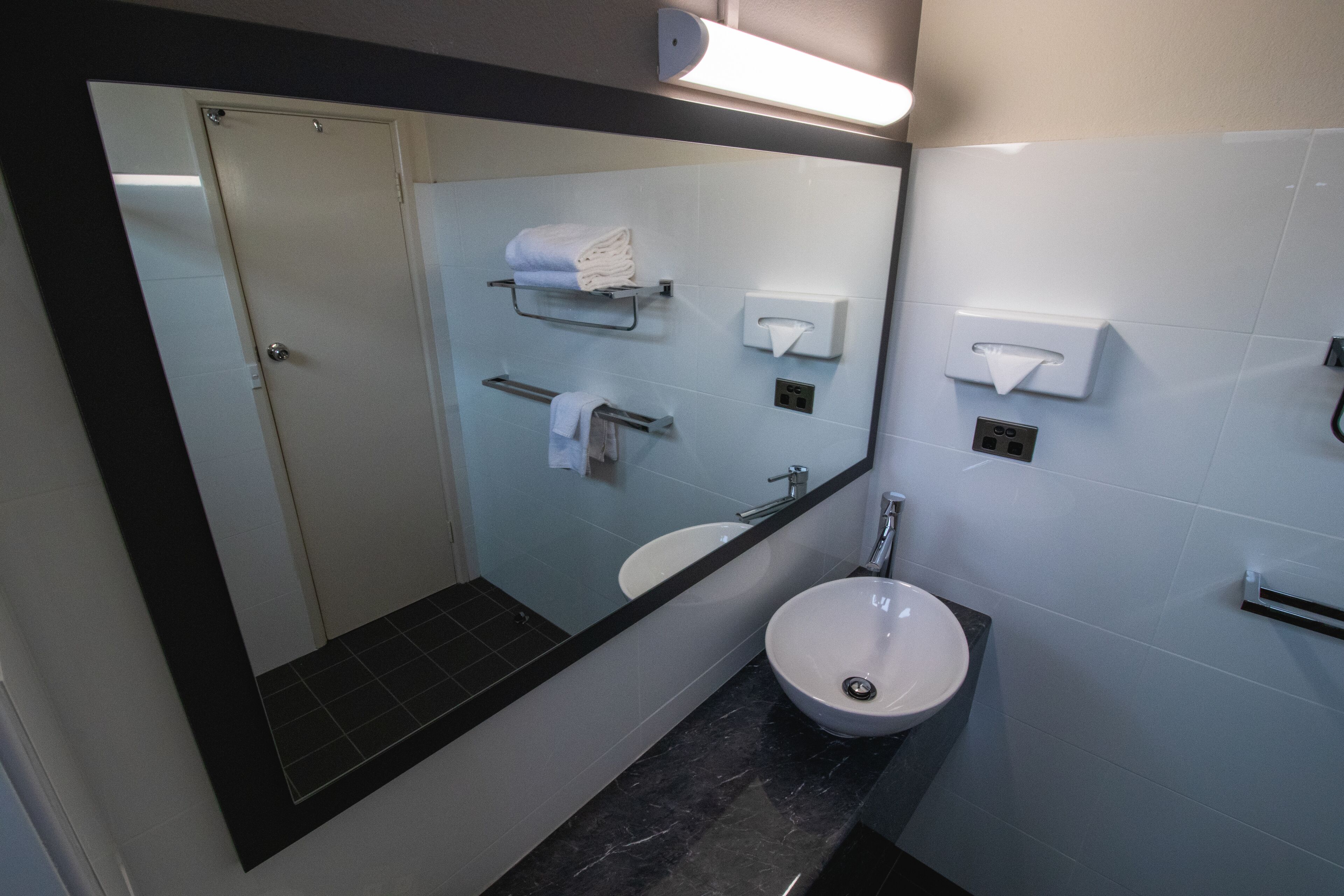 Un bagno moderno con uno specchio grande, un lavandino, un water e distributori di asciugamani.