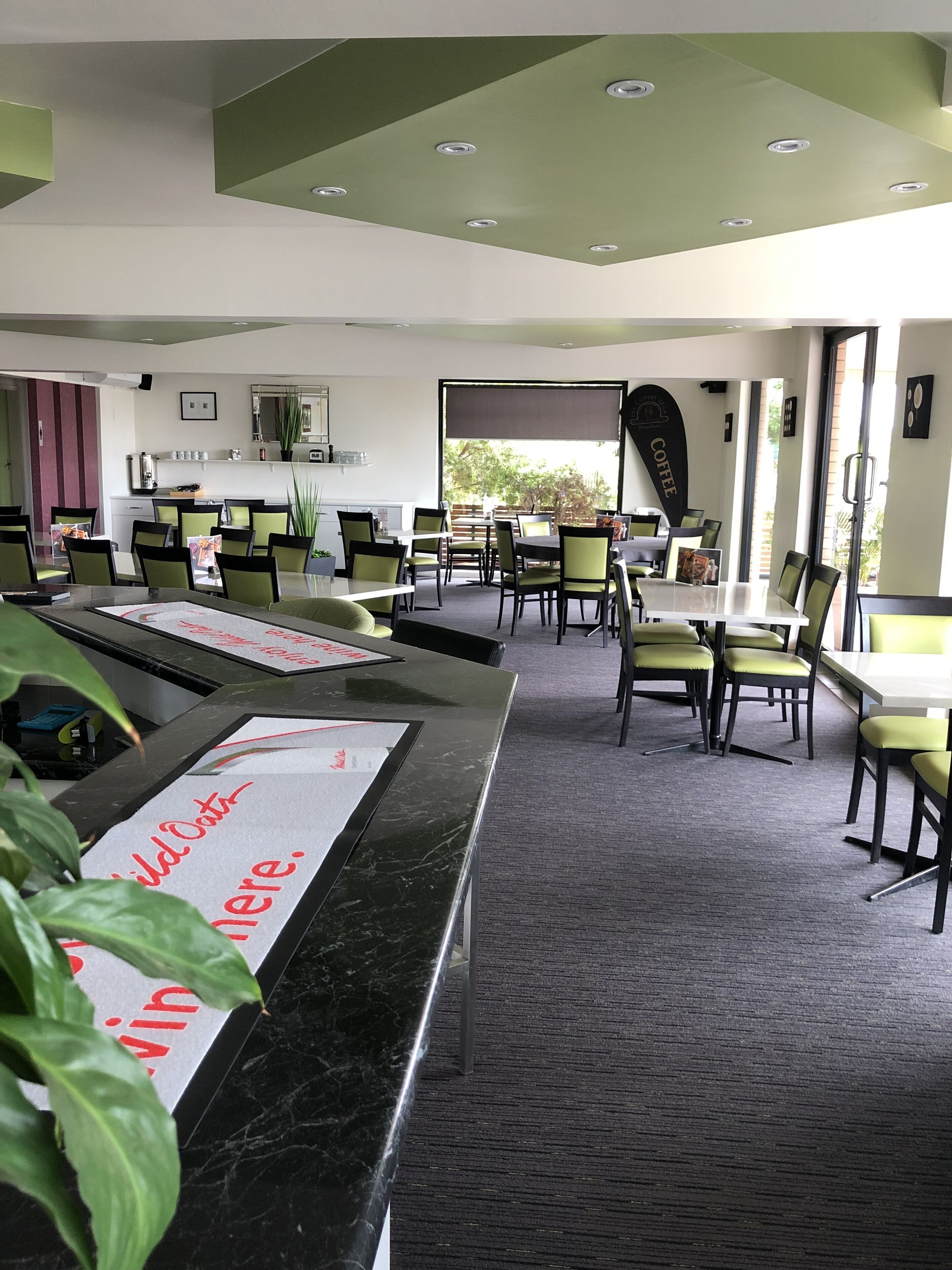 Un comedor moderno con sillas verdes, mesas de mármol y un amplio ventanal con vistas al exterior.