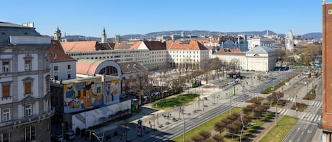 A cityscape with a prominent building featuring a large mural, a wide boulevard, and a clear blue sky.