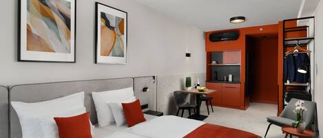 A modern hotel room with a large bed, a desk, a chair, and a wardrobe.