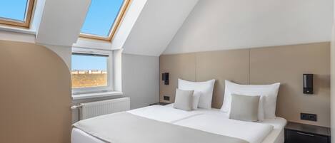 Une chambre avec un puits de lumière, un lit avec du linge de lit blanc, une table de chevet et une lampe fixée au mur.
