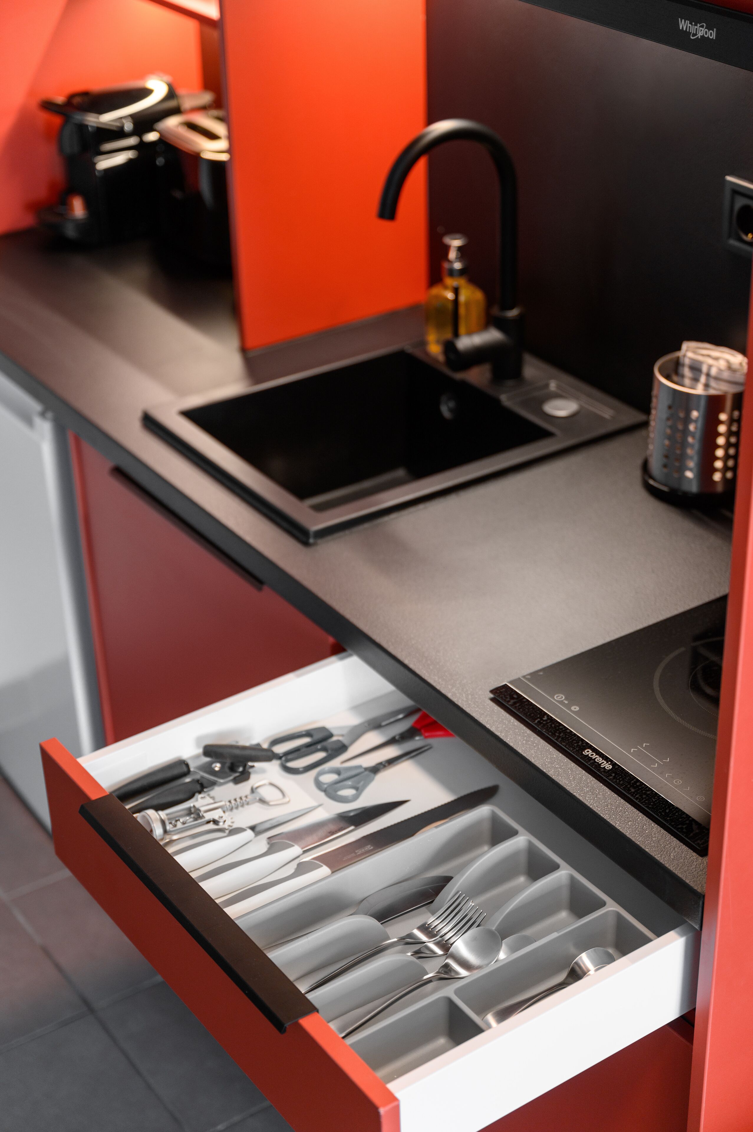 A kitchen with a modern design, featuring a black sink, a built-in stove, and a drawer with utensils.