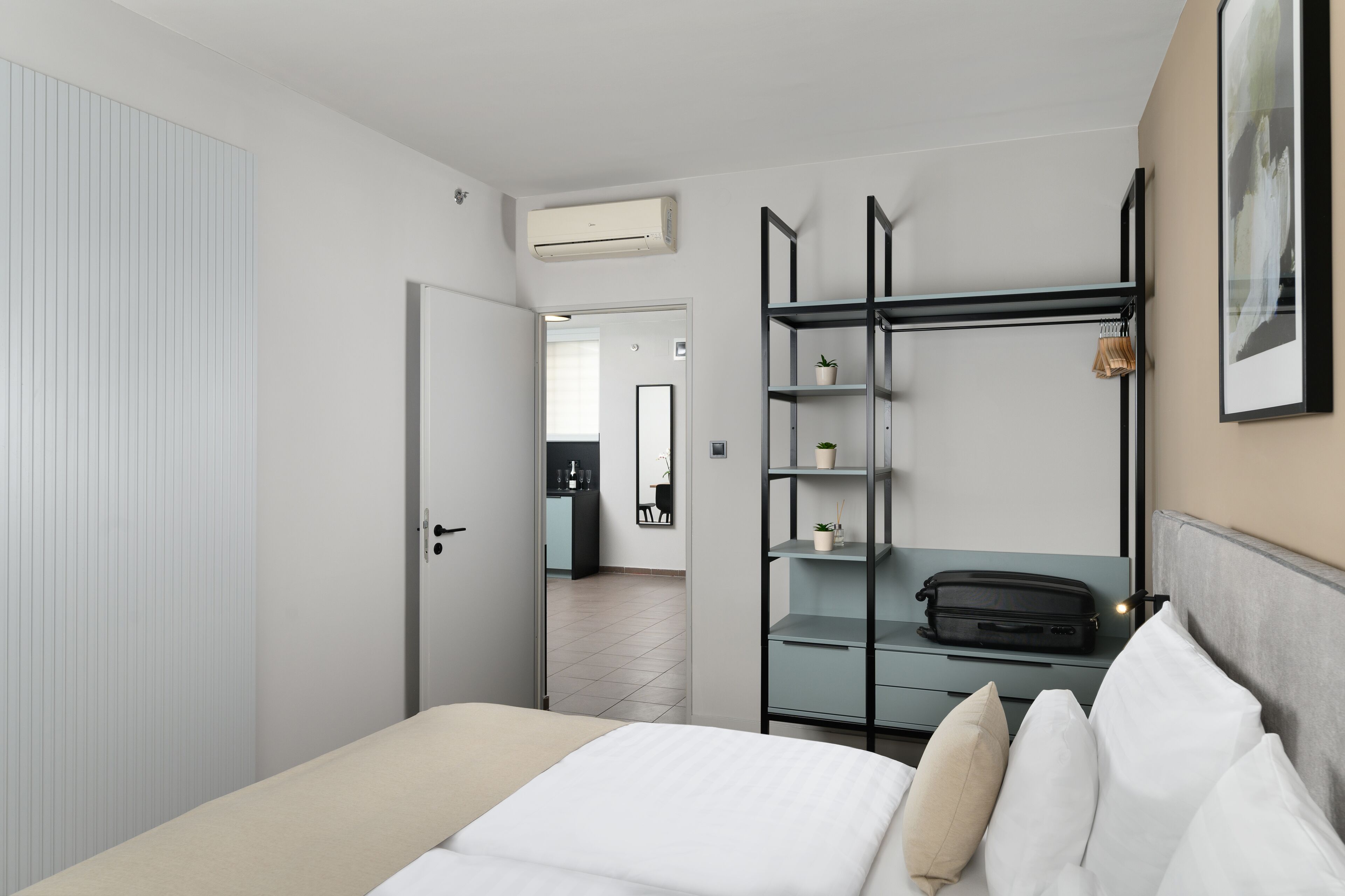 Una habitación de hotel moderna con una cama, un armario, un escritorio con silla y vistas al área de la cocina contigua.