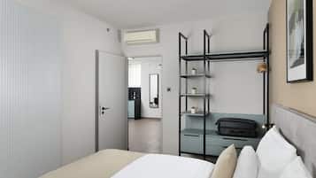 A modern hotel room with a bed, a wardrobe, a desk with a chair, and a view into the adjacent kitchen area.
