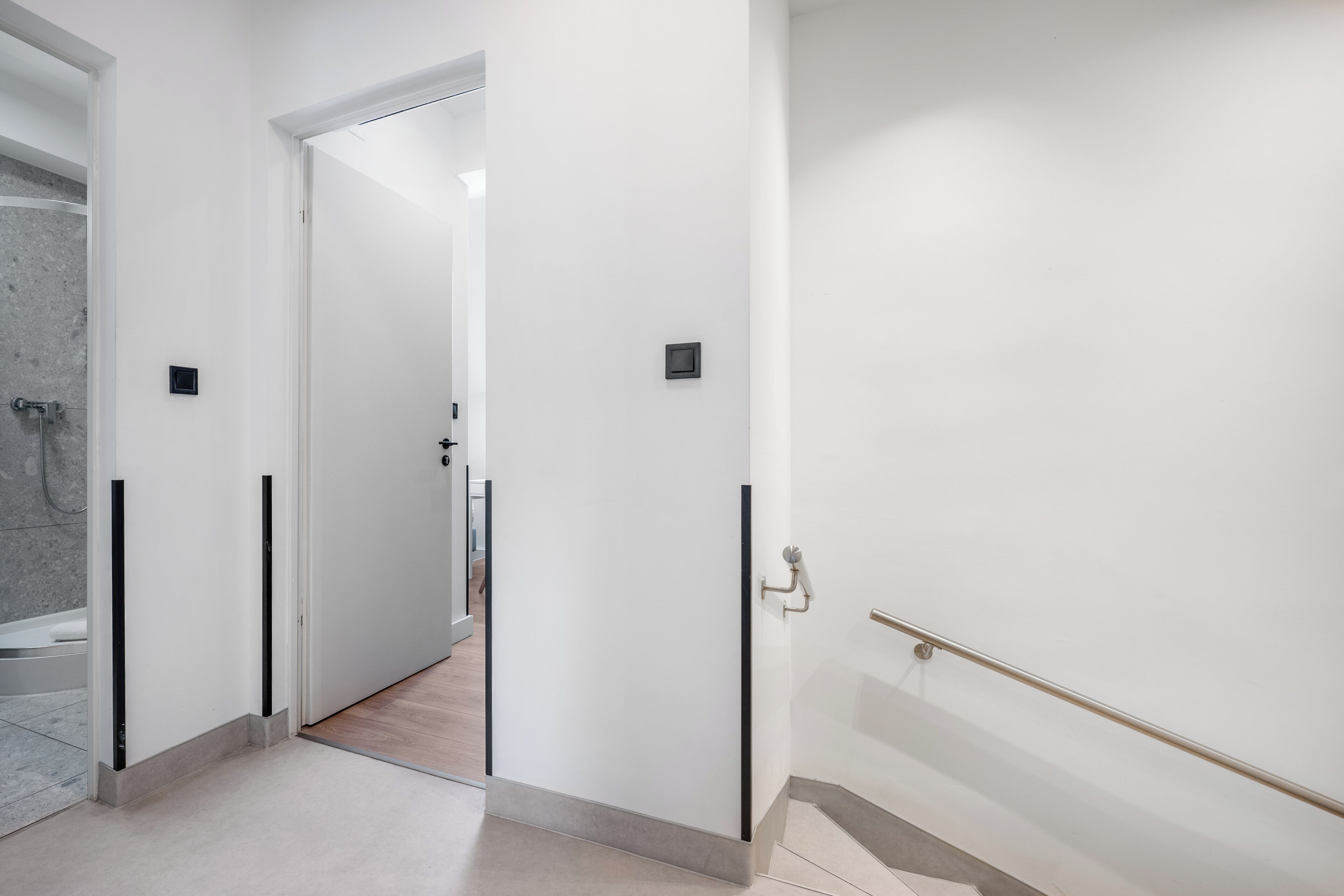 A modern hallway with white walls, a marble-tiled shower area, and a door leading to another room.