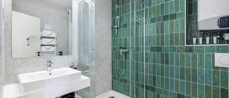 Un baño moderno con ducha envuelta en vidrio, un lavamanos blanco y paredes con azulejos verdes.