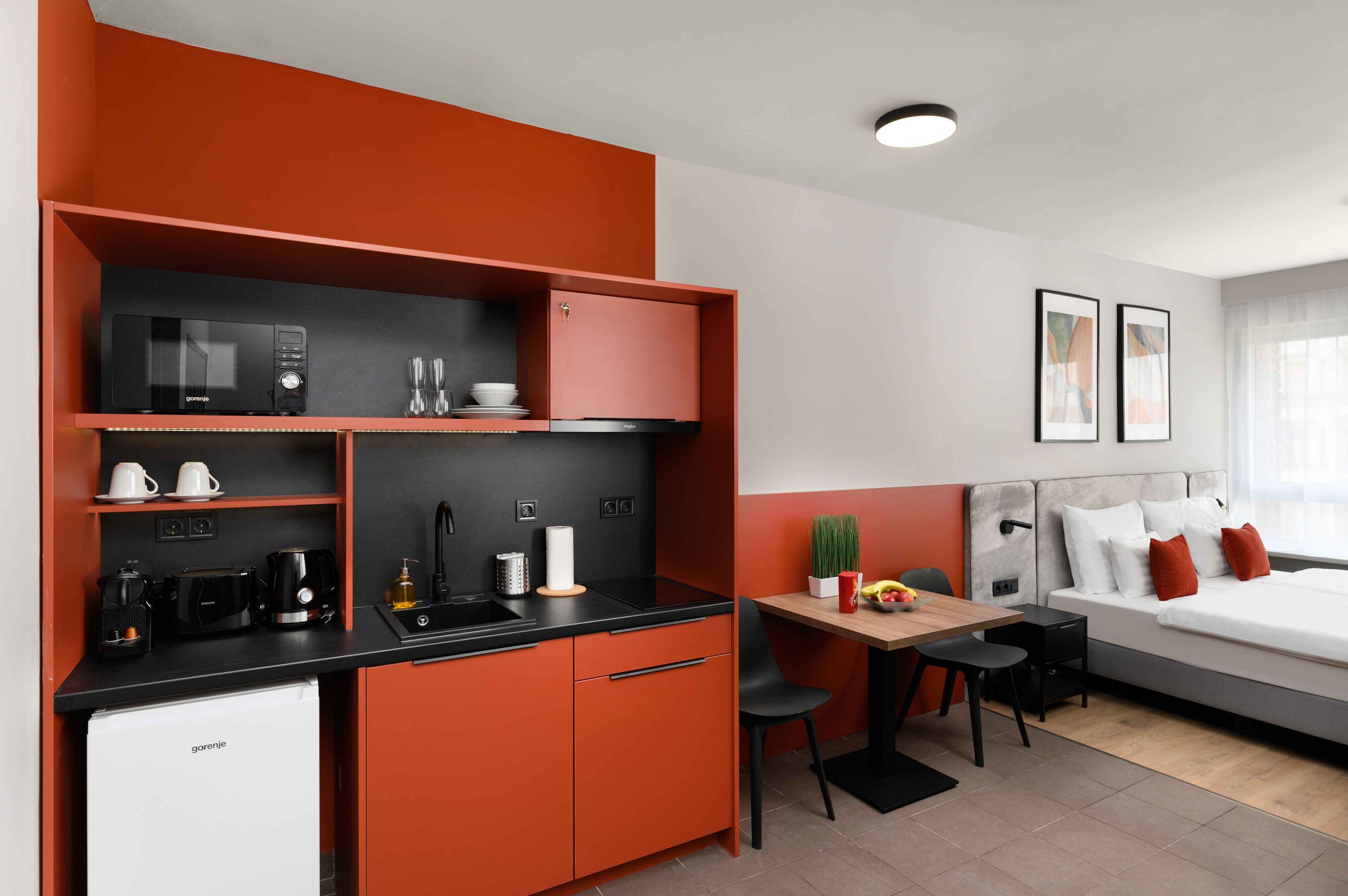 A compact hotel room with a kitchenette, a dining area, and a bed.