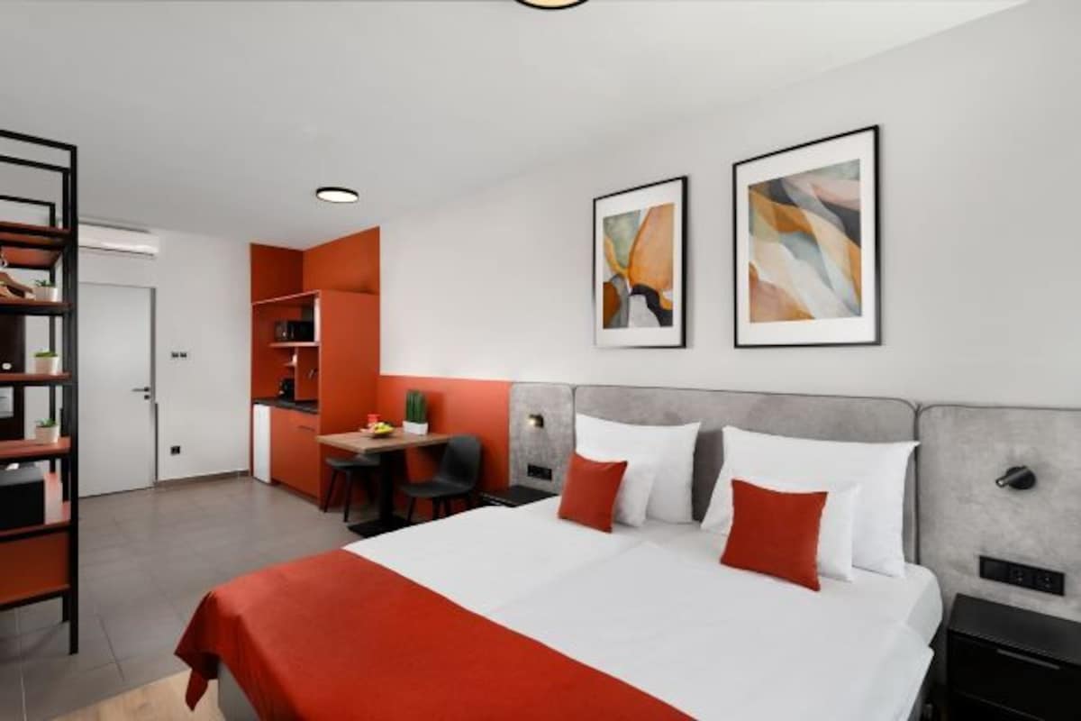 Una habitació d'hotel moderna amb un llit gran, una taula de treball i una cuineta.