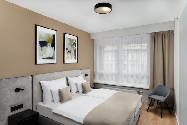 A modern hotel room with a large bed, a bedside table, a chair, and two abstract paintings on the wall. - Florin Apart Hotel (Budapest)
