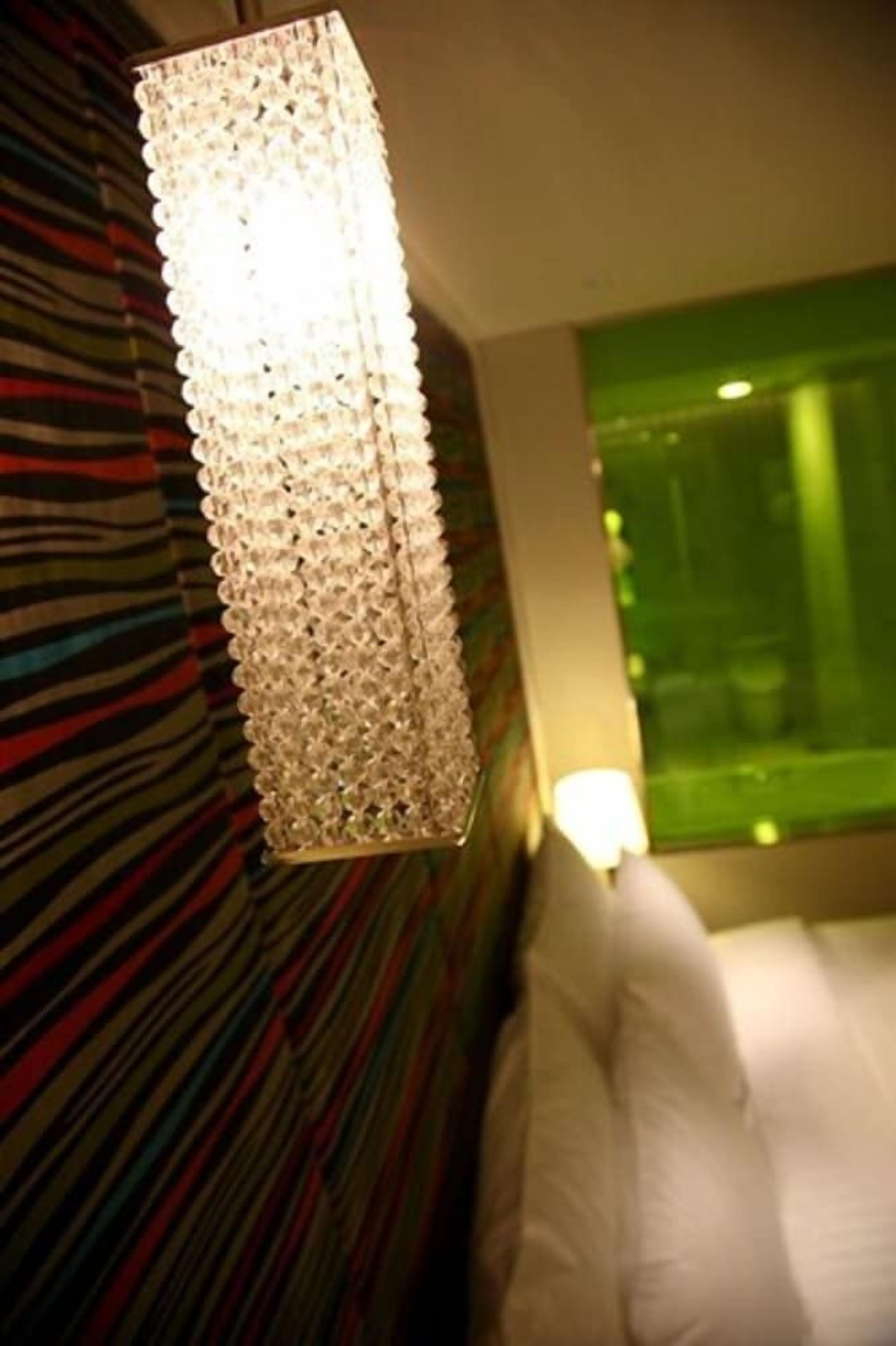 A room with a hanging light fixture, a striped wall, and a bed with white bedding.