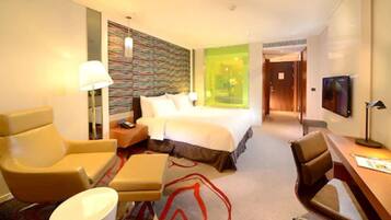 A hotel room with a bed, two armchairs, a desk, a lamp, and a television.