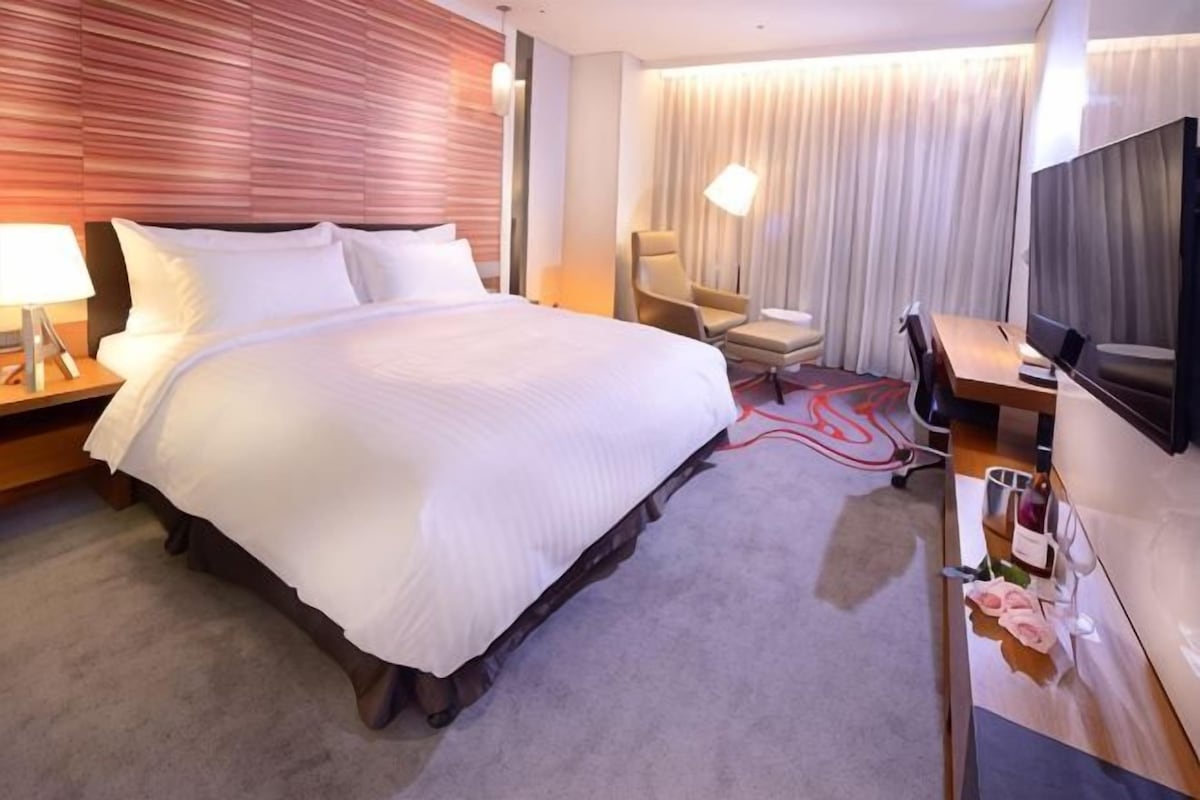 A hotel room with a large bed, a desk with a chair, a TV, and a lamp.