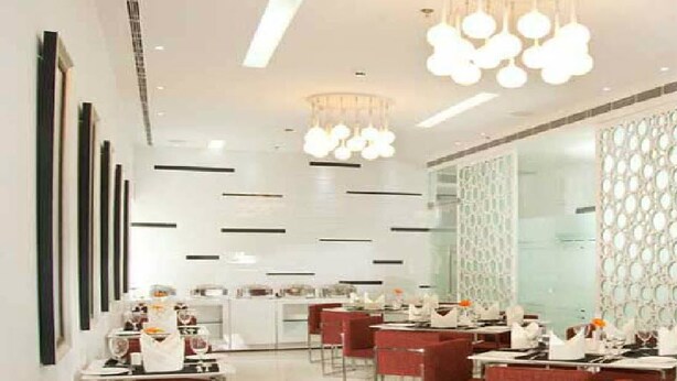 A modern restaurant with a clean, minimalist design, featuring a long dining area with tables and chairs, and decorative wall panels. - Sapphire Suites (Kolkata)