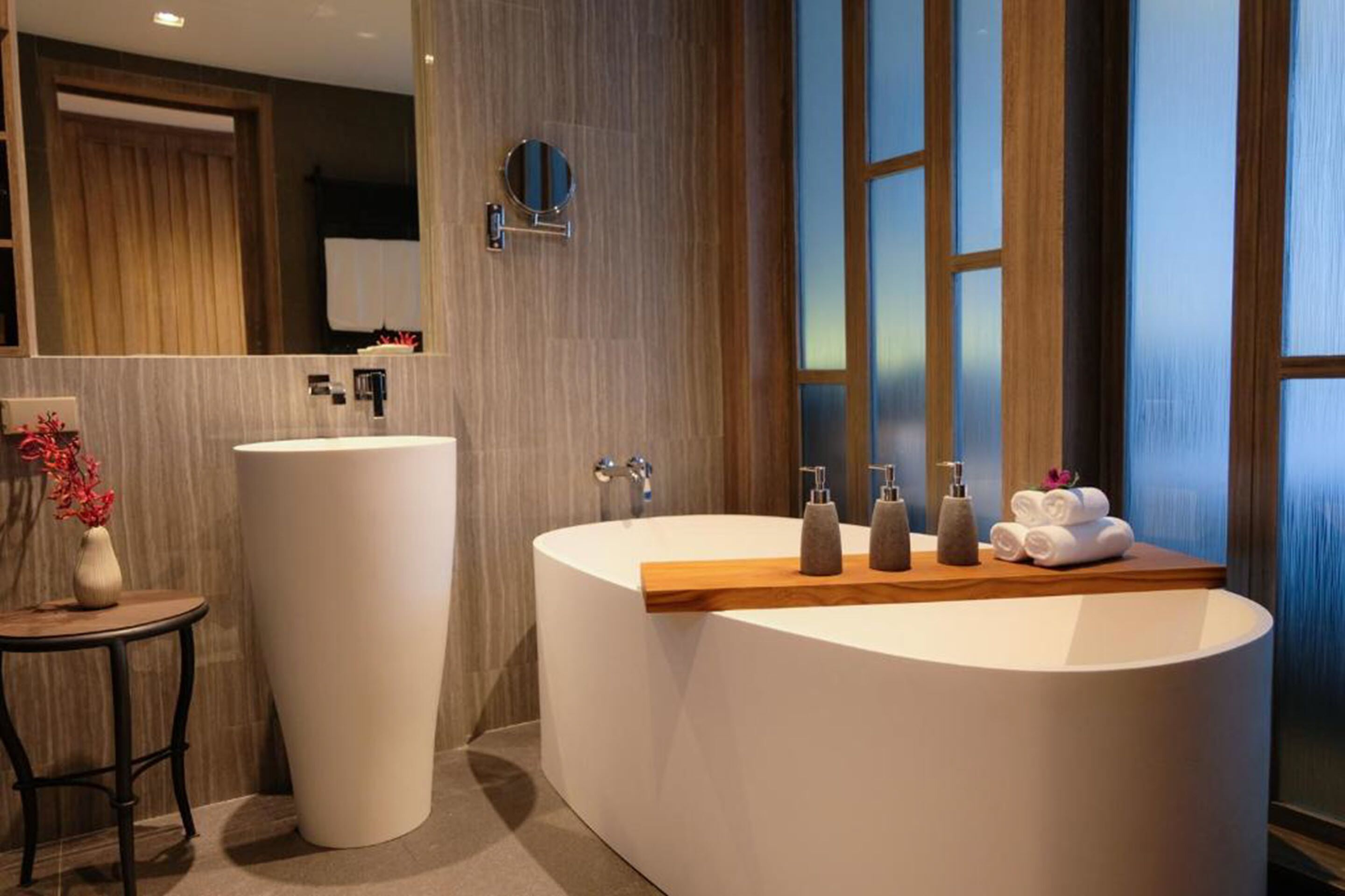 Un baño moderno con una bañera independiente, un tocador grande con espejo y una pequeña mesa con un florero.