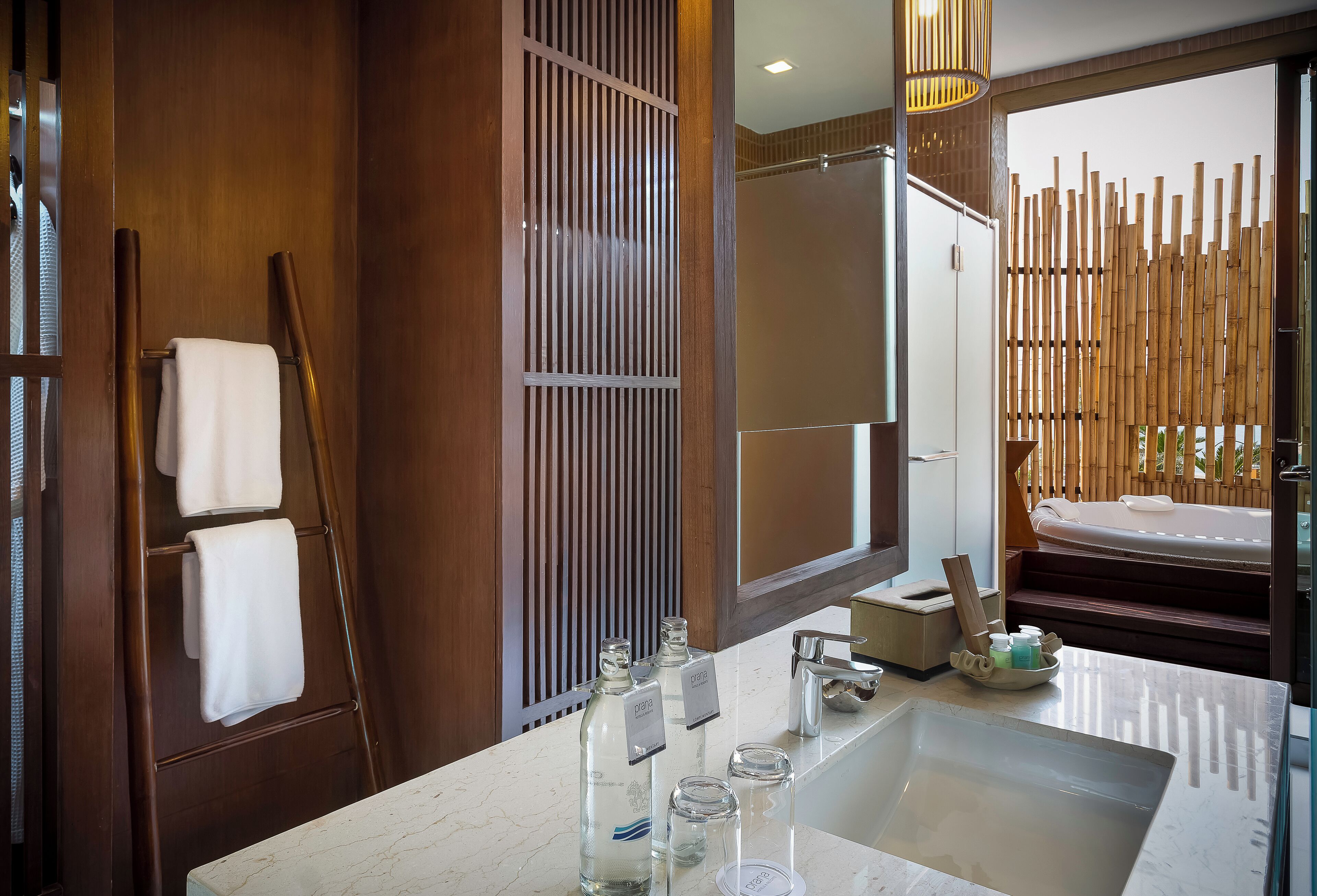 A modern bathroom with a large marble sink, a wooden towel rack, and a bamboo screen.
