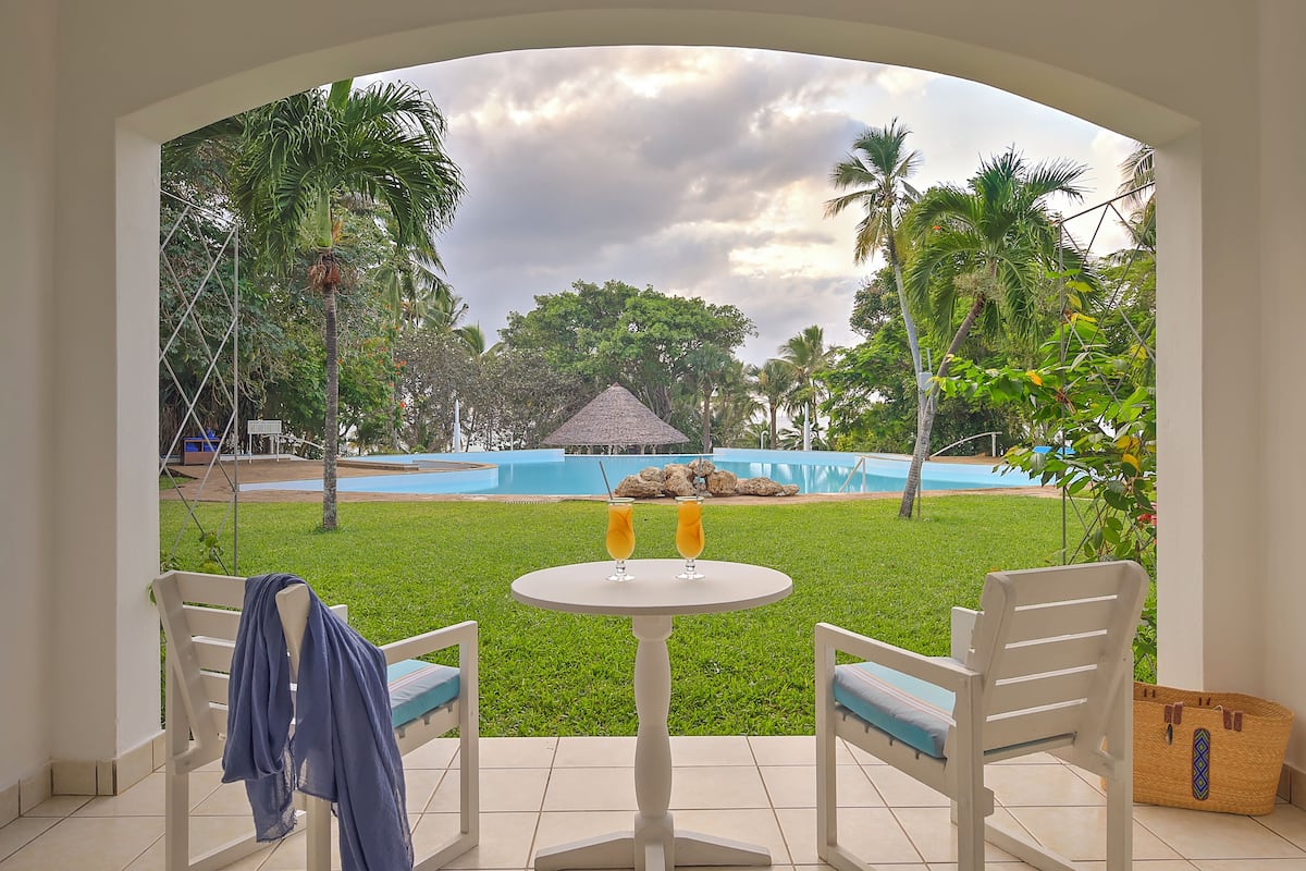 Une terrasse avec une table et deux chaises, donnant sur une piscine et une végétation luxuriante.