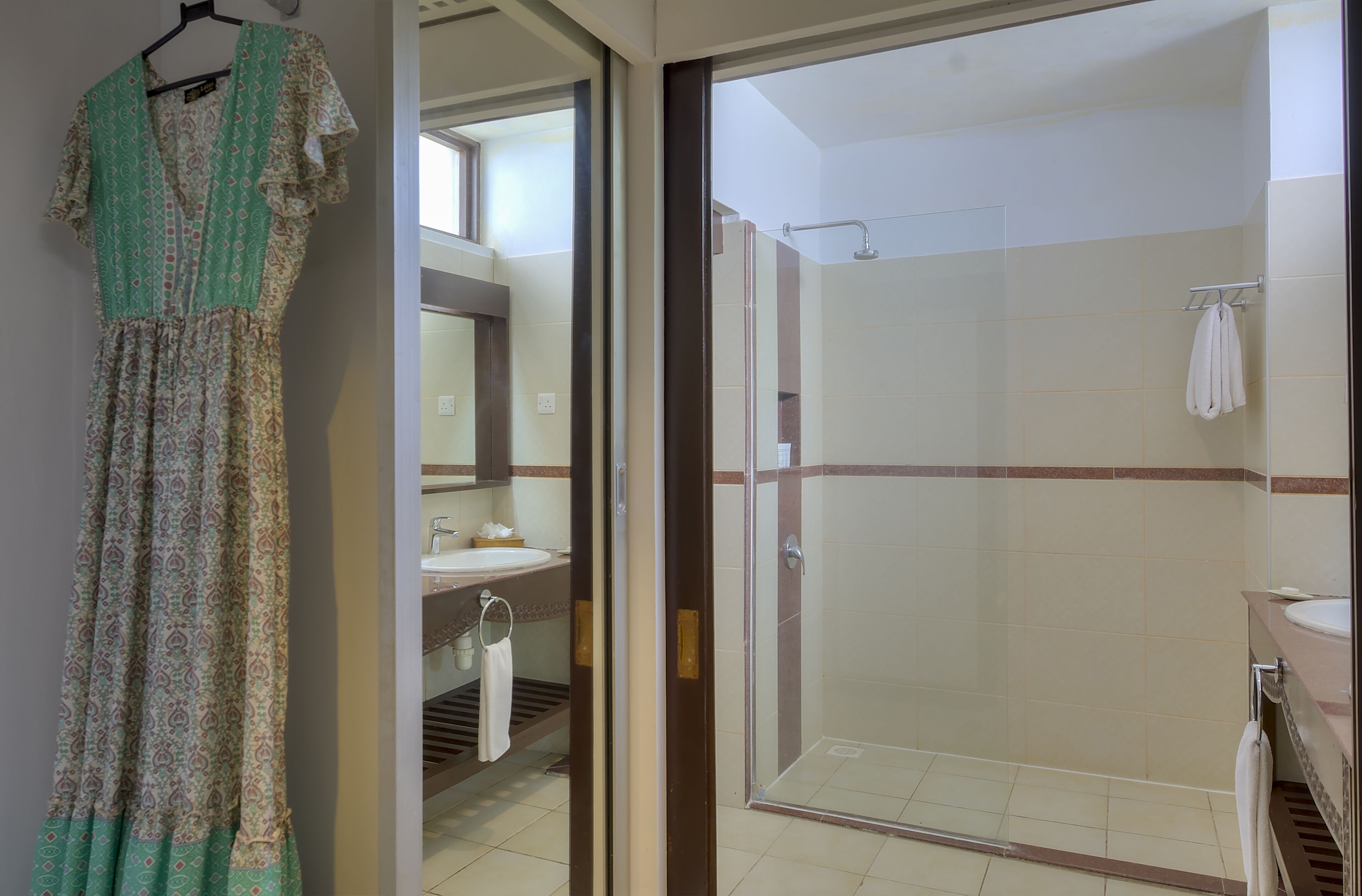 Een badkamer met douche, wastafel en een ophangende jurk.