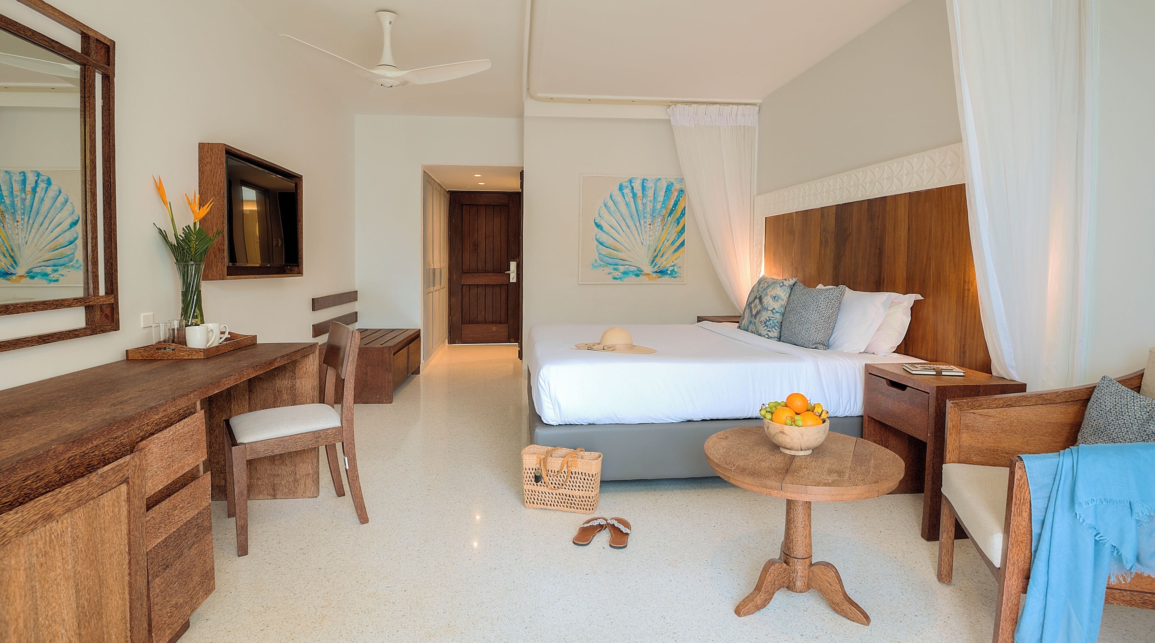 Habitación de hotel con cama, escritorio, silla, mesita con fruta y espejo.