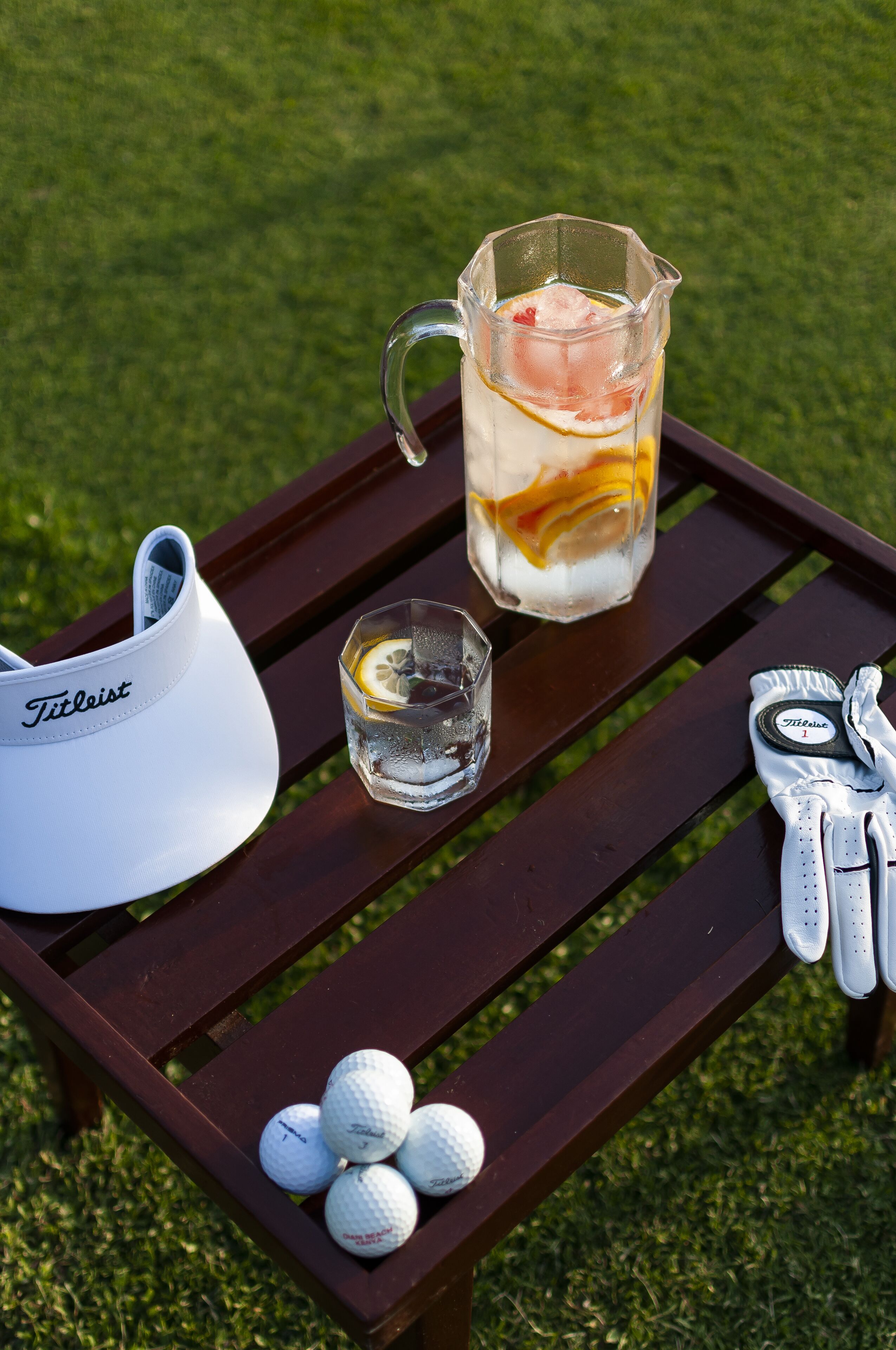 A golf bag, a glass pitcher with a drink, golf balls, and a golf glove on a wooden table.